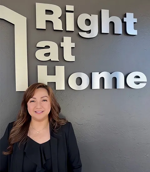 A woman with brown hair in a black shirt poses in front of the company logo.